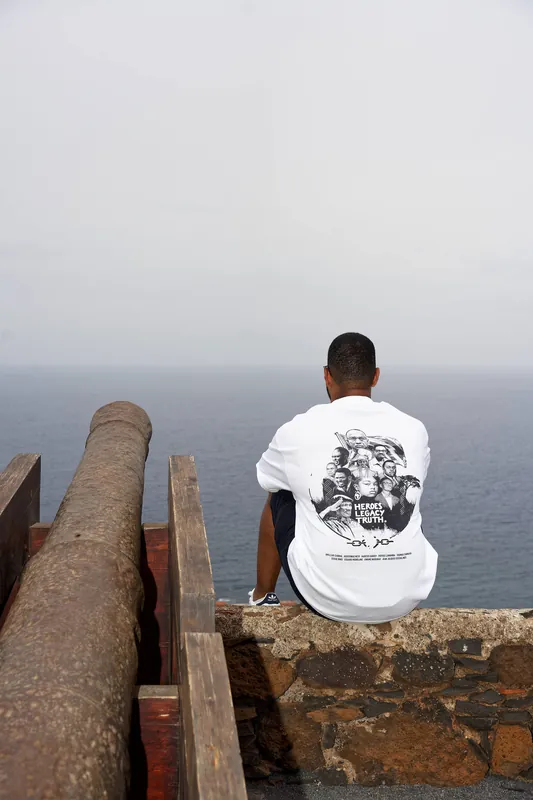 Seated on a fort wall by an old cannon, the shirt's back print facing the sea.
